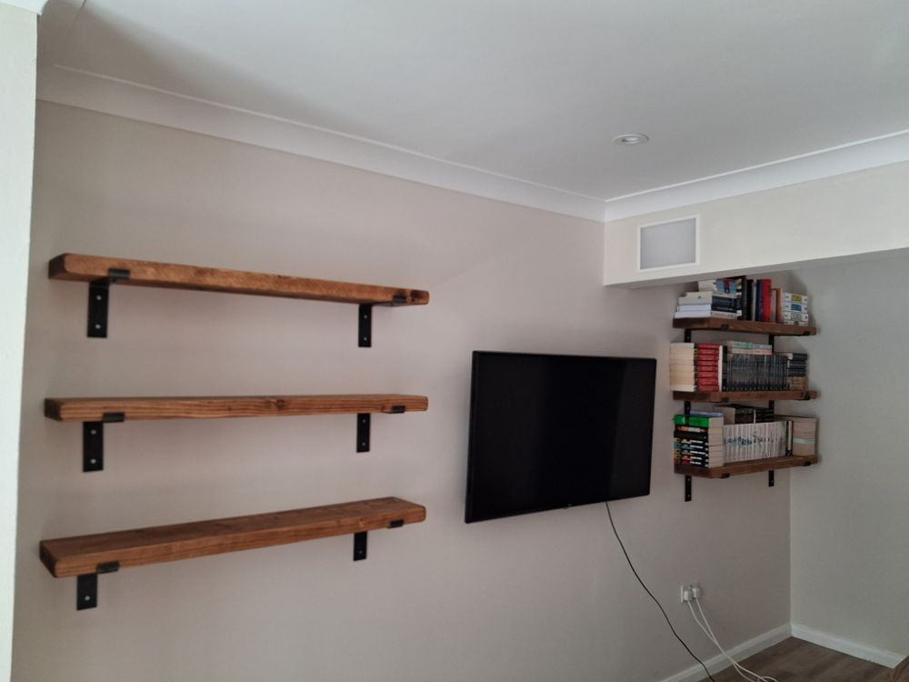 A living room after a visit: television on the wall, three shelves on one wall and three loaded bookshelves on another