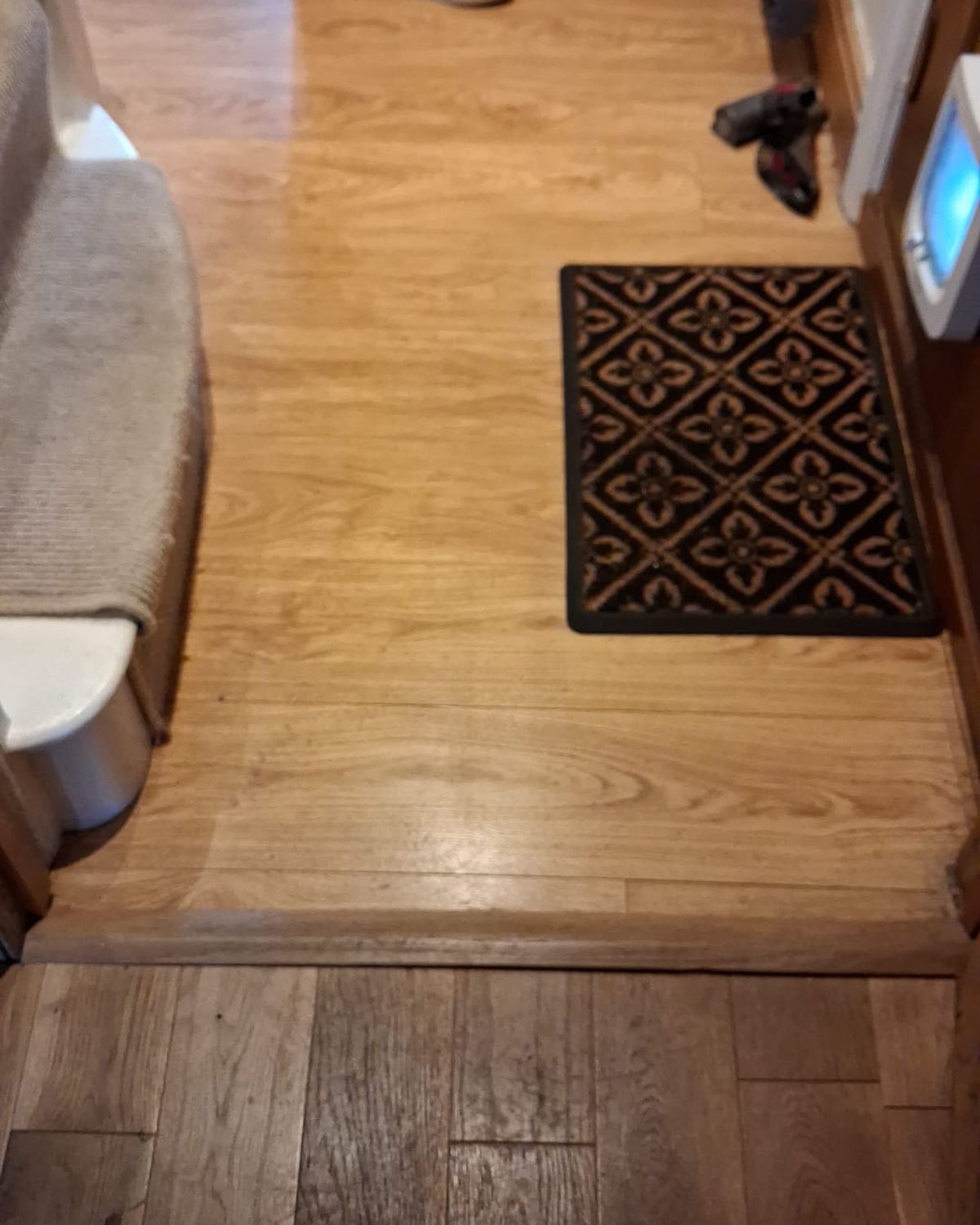 Before: the front-door end of a hallway with a laminate floor and a doormat