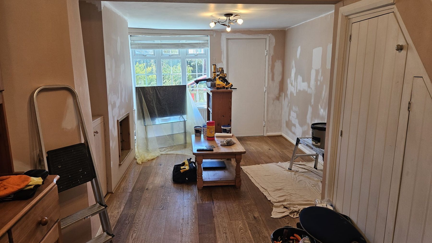 Before: the same living room with walls filled and sanded, floor sheeted, tools out