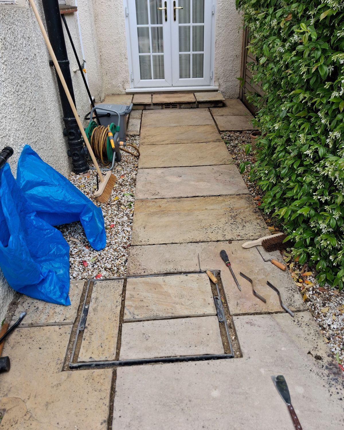 Before: a garden path with slabs lifted and a manhole frame being fitted