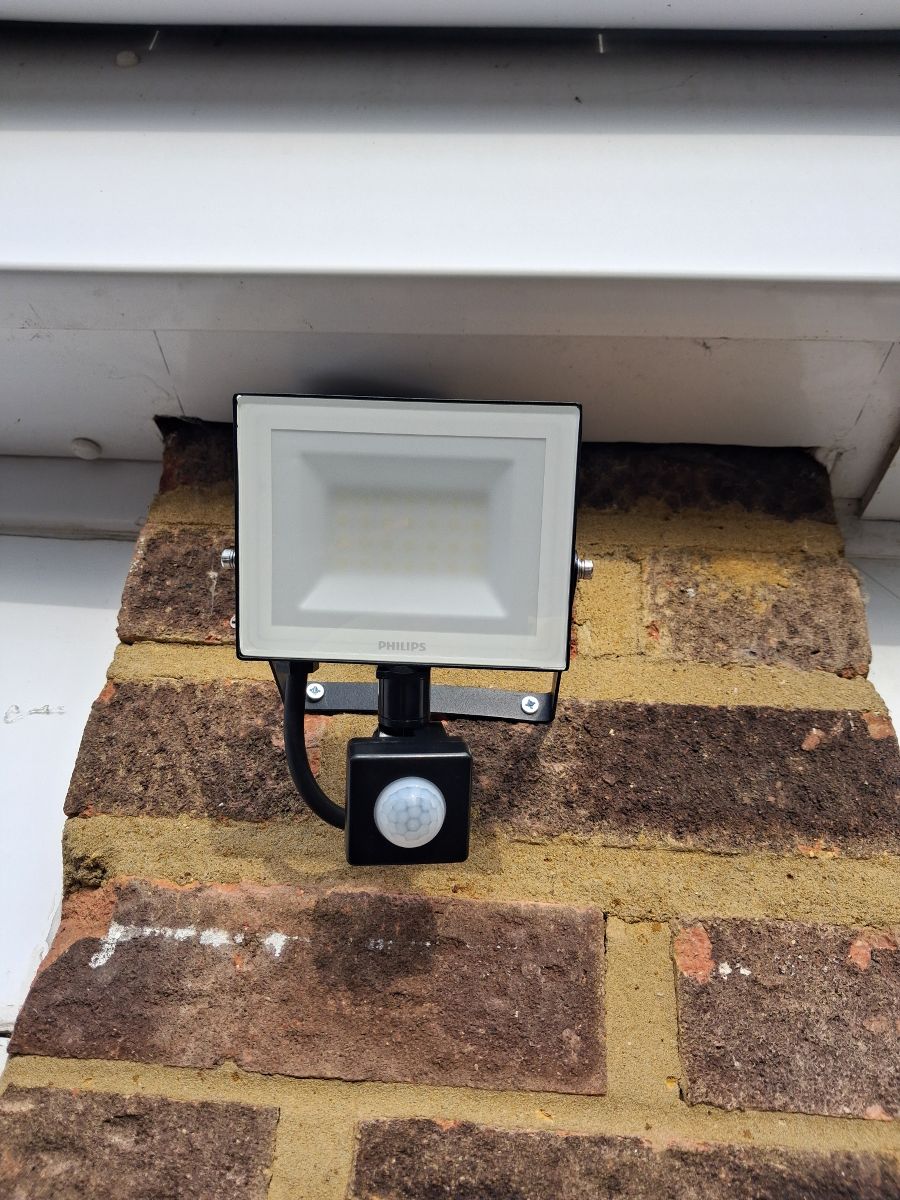 A new PIR security floodlight fitted to a brick wall under the eaves