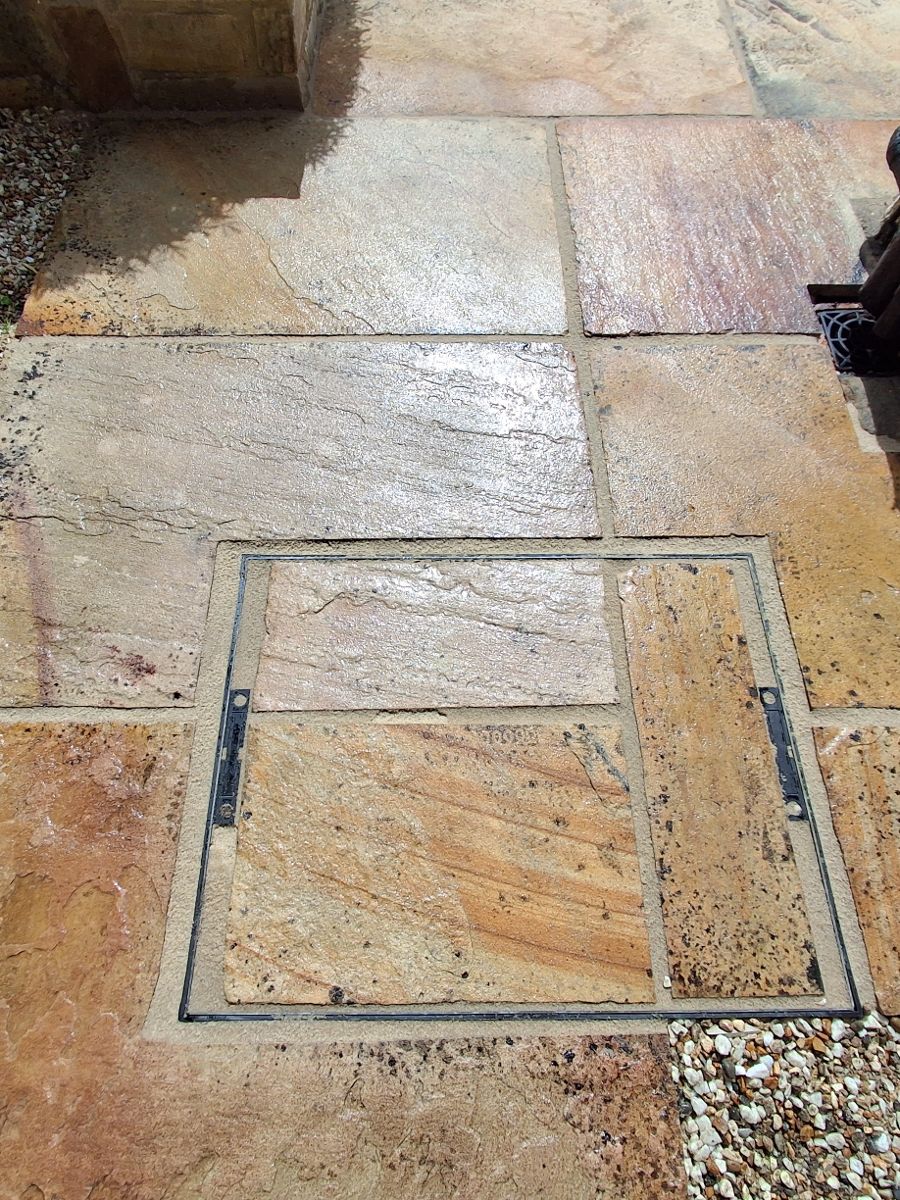 A recessed manhole cover set into a re-grouted sandstone patio